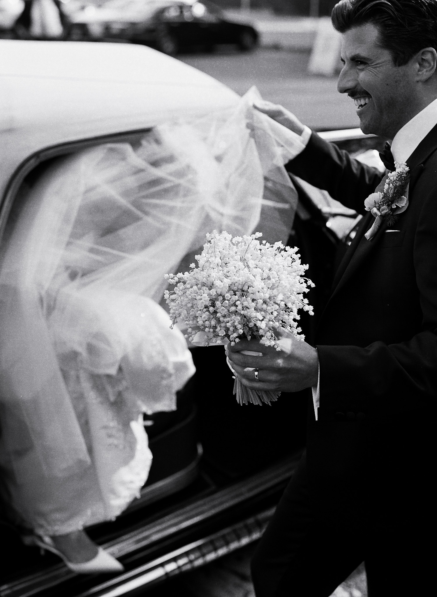 Black and white film image groom helping bride with veil